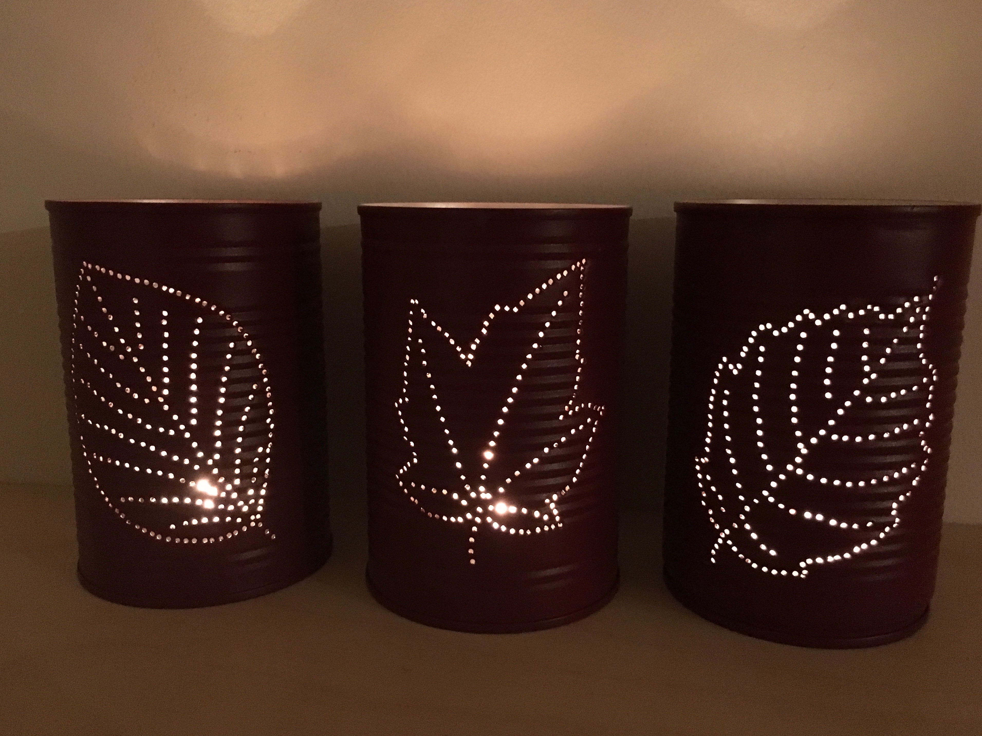 Three candle holders with leaf designs glow in a dark room