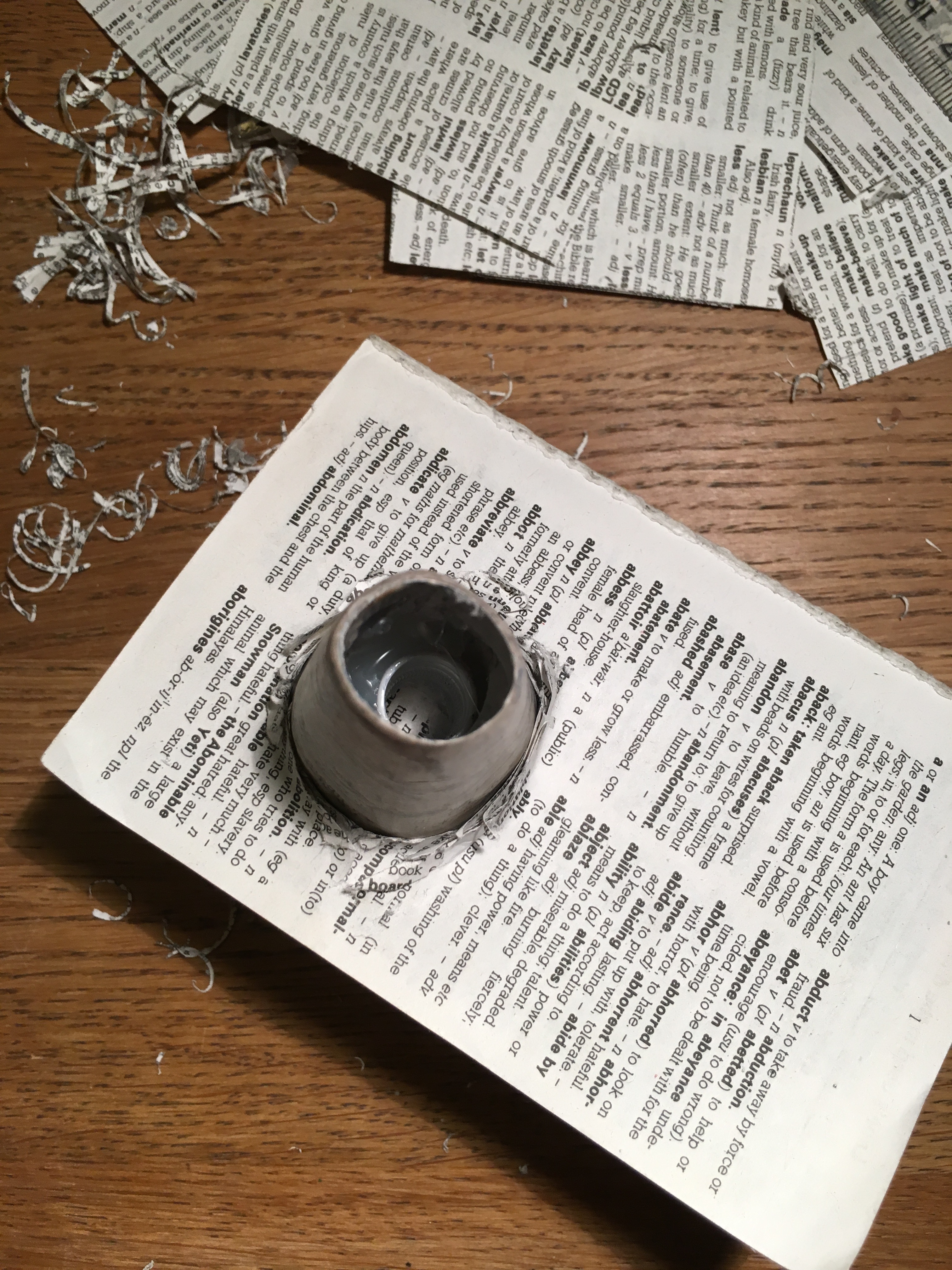 Looking down at a dictionary with a papier-mâché upright sticking out of it, surrounded by paper scraps