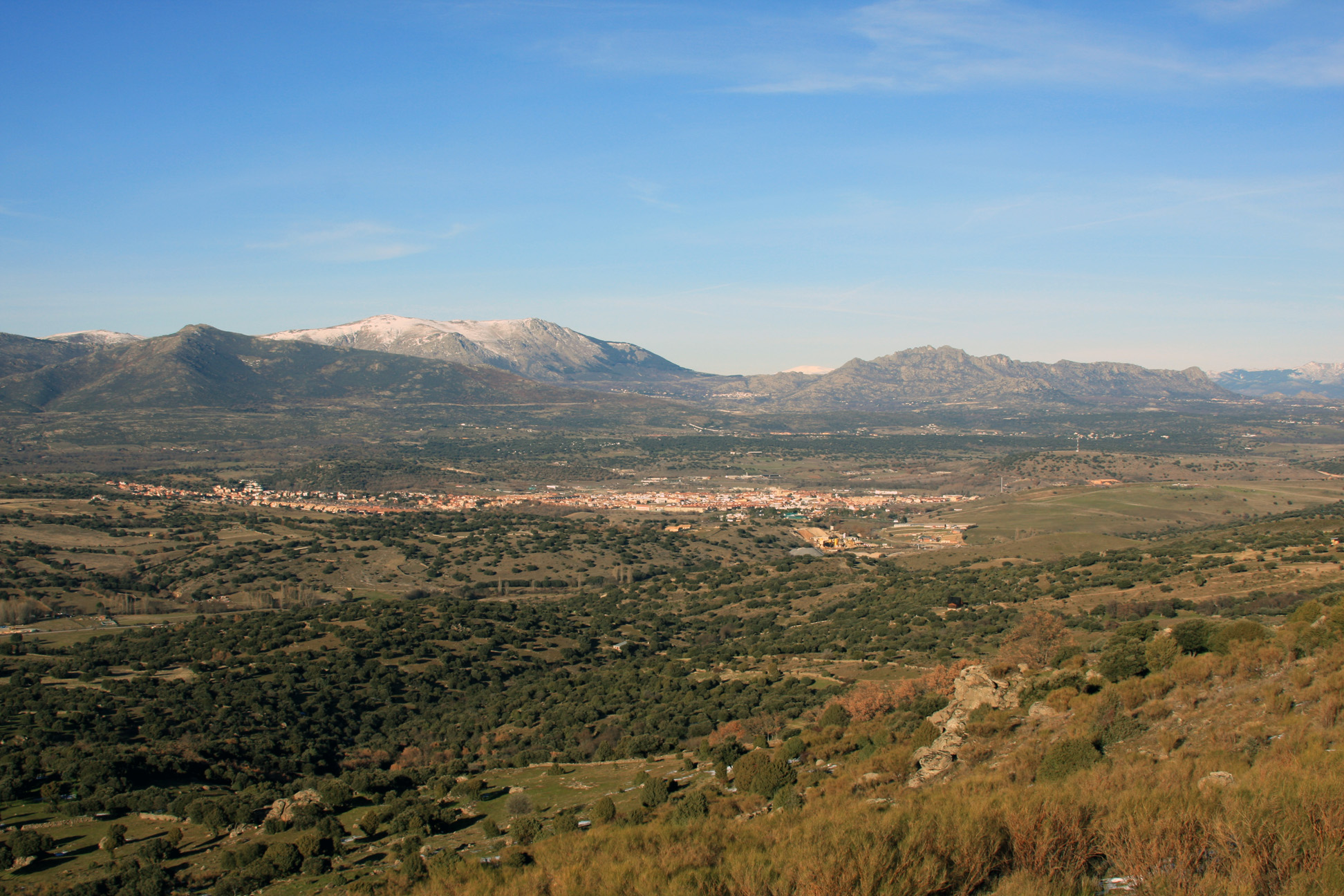 View over a sunny valley, with a town and mountains in the distance